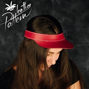 Könnte beinhalten: Ein roter Leder-Visier mit weißen Nähten. Das Visier wird von einer Person mit langen braunen Haaren getragen.