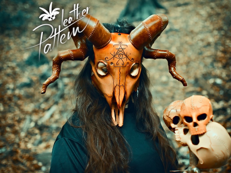 May include: A woman wearing a brown leather mask with horns and a skull design. The mask has a symbol with an eye and a triangle on the forehead. The woman is holding two small skulls in her hands.