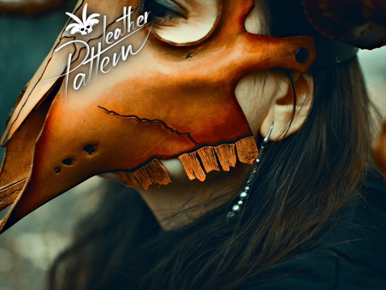 May include: A close-up of a person wearing a brown leather mask with a skull design. The mask has a fringe detail and is worn over the person's eyes. The person has long brown hair and is wearing a black shirt.