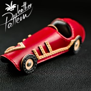 K&ouml;nnte beinhalten: Ein handgefertigtes rotes Leder-Spielzeugauto mit goldenen und schwarzen Akzenten. Der Rennwagen im Vintage-Stil hat detaillierte N&auml;hte und ein klassisches Design. Der Text "Leather Pattern" ist enthalten.
