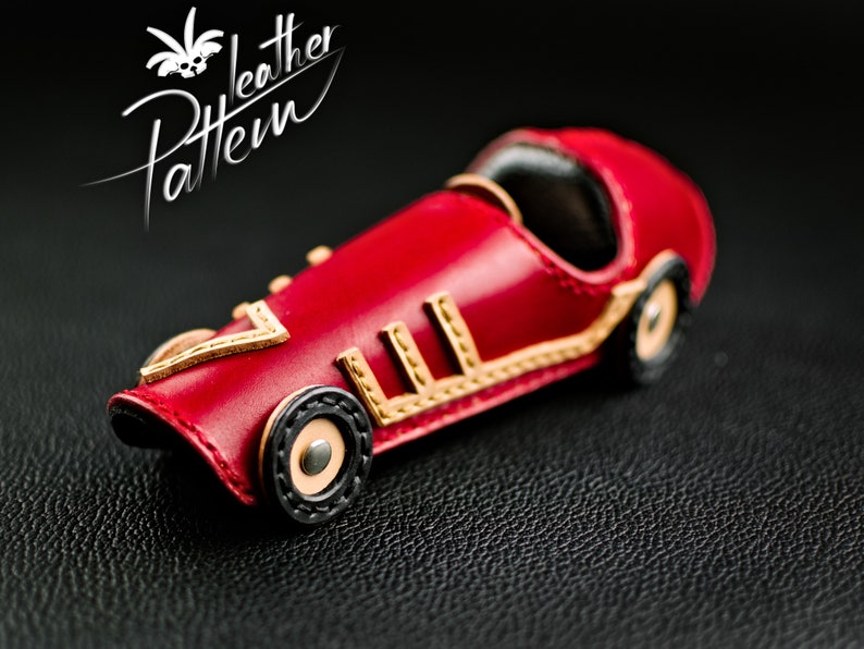 K&ouml;nnte beinhalten: Ein handgefertigtes rotes Leder-Spielzeugauto mit goldenen und schwarzen Akzenten. Der Rennwagen im Vintage-Stil hat detaillierte N&auml;hte und ein klassisches Design. Der Text "Leather Pattern" ist enthalten.