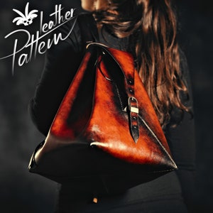 Può includere: Una borsa tote in pelle marrone con una tracolla nera e una fibbia dorata. La borsa ha un aspetto vissuto e viene indossata sulla spalla.