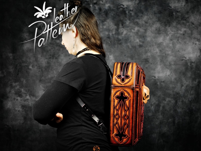 May include: A brown leather backpack with intricate black stitching and a decorative skull design. The backpack has a flap closure and a zipped pocket on the front.
