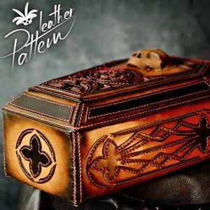 May include: A brown leather coffin-shaped box with intricate red stitching and a skull-shaped top. The box is decorated with a geometric pattern and has a black leather interior.