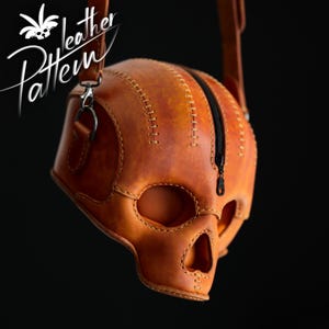 Könnte beinhalten: Eine hellbraune Ledertasche in Form eines menschlichen Schädels mit sichtbaren Nähten entlang der Kanten und einem schwarzen Reißverschluss in der Mitte. Die Tasche hat einen Riemen und zeigt den Text "leather Pattern" mit einem Totenkopf-Symbol.