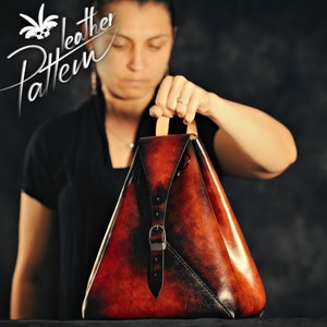 Op de afbeelding: Een bruine, driehoekige leren tas met een gespsluiting en een band. De tas is gemaakt van verweerd leer en heeft een vintage uitstraling.