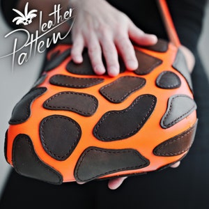 May include: A bright orange leather bag with brown leather patches sewn on in a unique pattern. The bag is held in a hand.