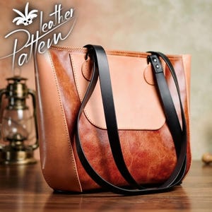 Puede incluir: Un bolso tote de cuero bicolor con una sección superior de color tostado claro liso y una parte inferior de cuero texturizado y desgastado en tono marrón rojizo. Incluye dos correas negras largas sujetas con remaches.