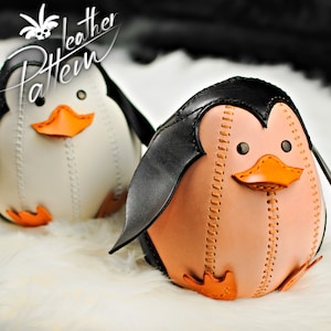 Könnte beinhalten: Zwei handgefertigte Lederpinguin-Figuren. Einer ist weiß mit schwarzen Flügeln, der andere pfirsichfarben mit schwarzen Flügeln. Beide haben orangefarbene Schnäbel und Füße und sind mit kontrastierendem Faden genäht. Der Text "Leather Pattern" befindet sich in der oberen linken Ecke.