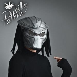 K&ouml;nnte beinhalten: Eine silberne Predator-Maske mit schwarzem Netzvisier und Dreadlocks. Die Maske ist aus Leder und hat ein gen&auml;htes Design.