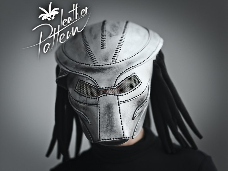 K&ouml;nnte beinhalten: Eine silberne Predator-Maske aus Leder mit schwarzen Dreadlocks. Die Maske hat ein detailliertes Design mit gen&auml;hten Linien und Maschen-Augenabdeckungen.