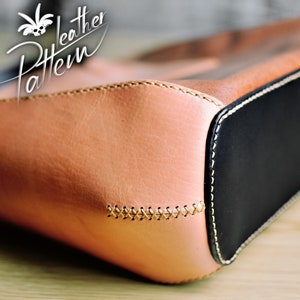 Puede incluir: Un bolso de cuero color canela con un panel base de cuero negro, detalles de punto de cruz visibles en hilo claro a lo largo de la costura lateral y un logotipo blanco en la esquina superior izquierda que dice Leather Pattern.