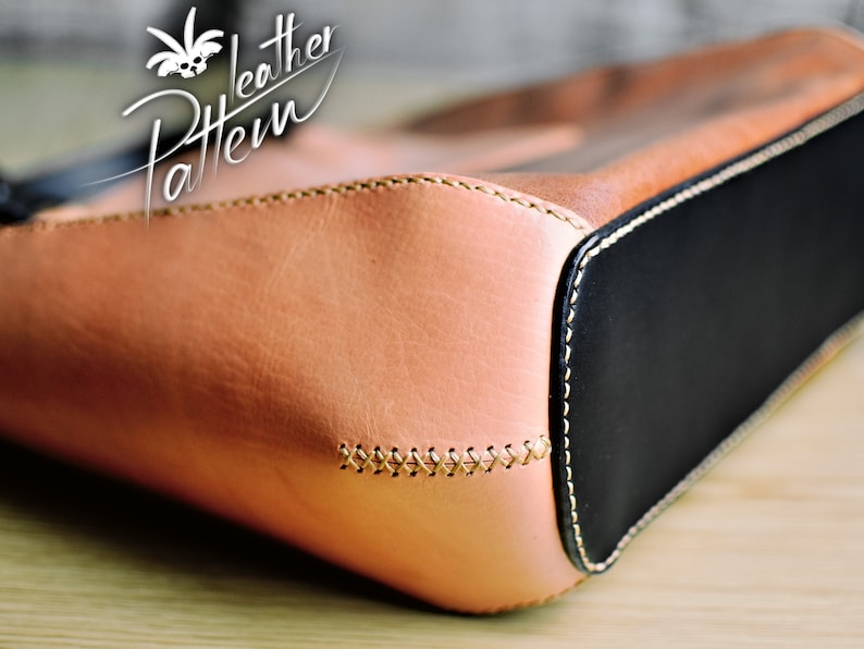 Puede incluir: Un bolso de cuero color canela con un panel base de cuero negro, detalles de punto de cruz visibles en hilo claro a lo largo de la costura lateral y un logotipo blanco en la esquina superior izquierda que dice Leather Pattern.