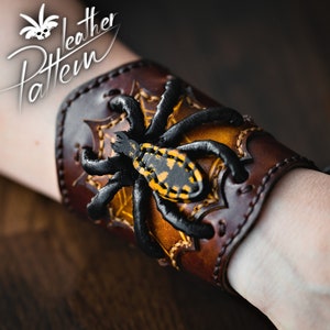 May include: A brown leather bracelet with a black and yellow spider design. The bracelet is adjustable and has a lace-up closure.