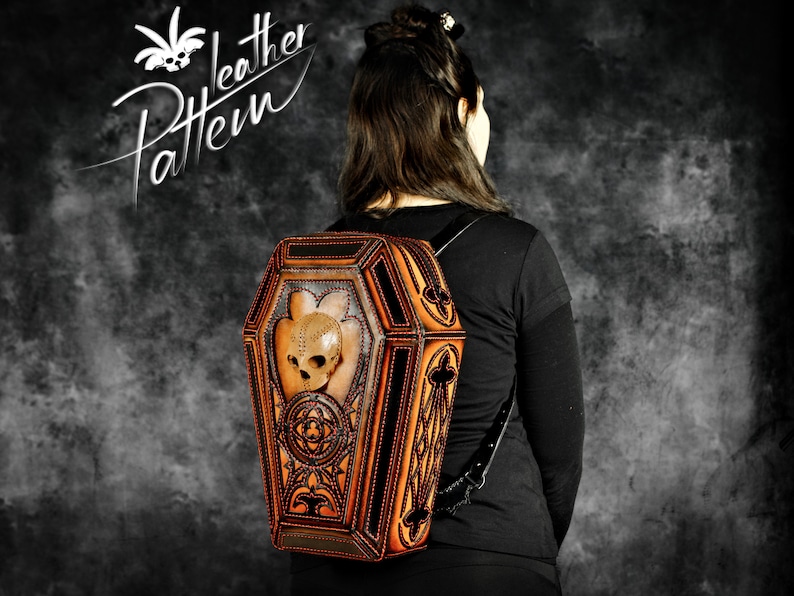 May include: A brown leather backpack shaped like a coffin with a skull design and metal accents. The backpack has a black strap and is being worn by a person.