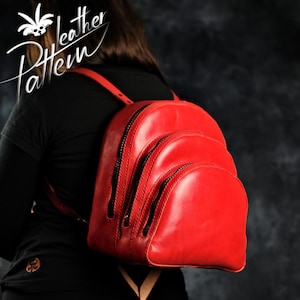 Könnte beinhalten: Ein roter Lederrucksack mit drei Fächern und Reißverschlüssen. Der Rucksack wird von einer Person getragen.