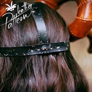 May include: Back view of a black leather headband with a distressed finish and silver rivets. The headband has a wide band and two straps that cross over the top of the head. The headband is worn by a person with long dark hair.