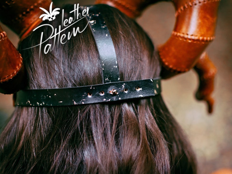 May include: Back view of a black leather headband with a distressed finish and silver rivets. The headband has a wide band and two straps that cross over the top of the head. The headband is worn by a person with long dark hair.