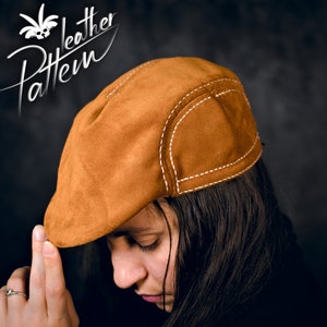 Puede incluir: Un gorro de cuero marrón de gamuza con costuras blancas. El gorro lo lleva una persona con el pelo largo y castaño.