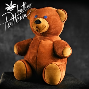 May include: A brown teddy bear with blue eyes and a brown nose. The bear is sitting on a black surface.