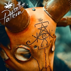 May include: A close-up of a brown leather mask with horns. The mask has a detailed design of a stylized eye and geometric shapes. The mask is worn by a person, but only the eyes are visible.