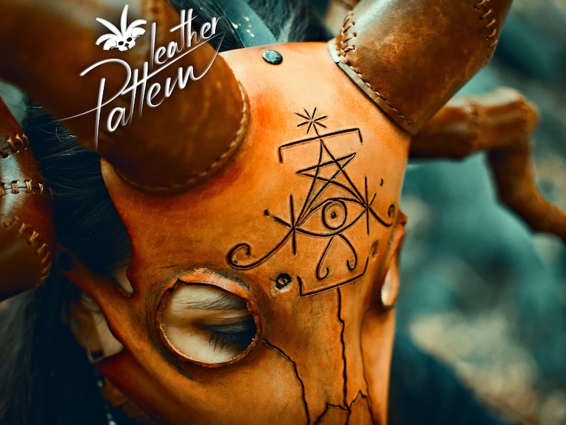 May include: A close-up of a brown leather mask with horns. The mask has a detailed design of a stylized eye and geometric shapes. The mask is worn by a person, but only the eyes are visible.