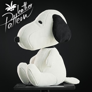 May include: A white plush Snoopy doll with black ears and nose, seated on a black surface. The words "Leather Pattern" are written in white script in the upper left corner. The doll is a popular cartoon character.