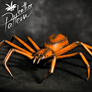 Peut inclure: Une grande sculpture d'araignée en cuir marron avec huit pattes et un corps détaillé. L'araignée est posée comme si elle rampait en avant.