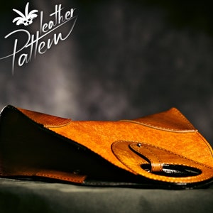 May include: A brown leather handbag with a unique design featuring a circular cutout and a buckle closure. The bag is lying on a dark surface.