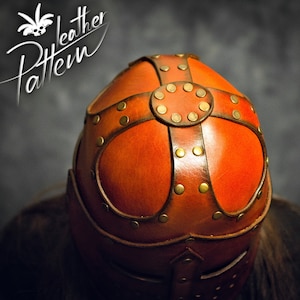 May include: A brown leather helmet featuring a cross-shaped overlay secured with brass-colored metal rivets. The top of the helmet displays a circular leather piece at the center of the cross. The text "Leather Pattern" is visible in the upper left.