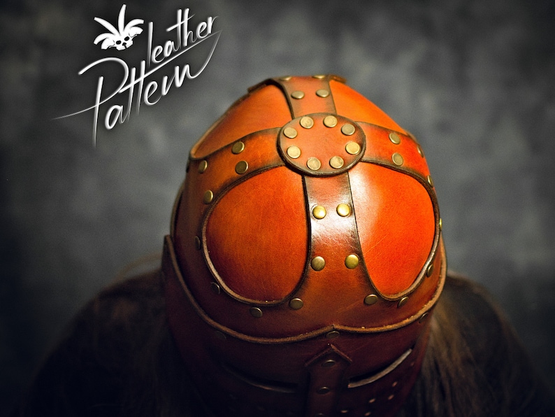 May include: A brown leather helmet featuring a cross-shaped overlay secured with brass-colored metal rivets. The top of the helmet displays a circular leather piece at the center of the cross. The text "Leather Pattern" is visible in the upper left.