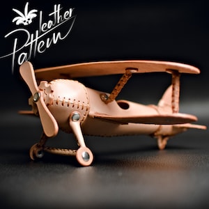 Peut inclure: Un avion en cuir marron modèle avec une hélice et des roues. L'avion est en cuir et a un design cousu. L'avion est sur un fond noir.