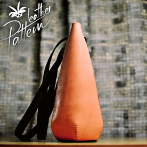 Puede incluir: Un bolso en forma de cono hecho de cuero color canela claro con una correa negra. El bolso presenta costuras visibles a lo largo de los bordes laterales y una abertura estrecha en la parte superior. El texto "Pattern Leather" est&aacute; impreso en blanco en la esquina superior izquierda.