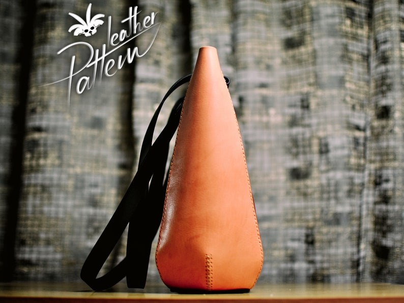 Puede incluir: Un bolso en forma de cono hecho de cuero color canela claro con una correa negra. El bolso presenta costuras visibles a lo largo de los bordes laterales y una abertura estrecha en la parte superior. El texto "Pattern Leather" est&aacute; impreso en blanco en la esquina superior izquierda.
