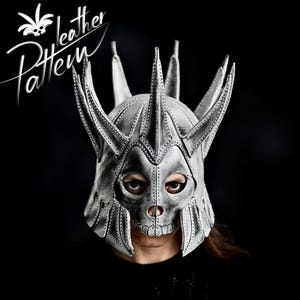 Könnte beinhalten: Eine silberne Totenkopfmaske mit einer spitzen Krone und filigranen Details. Die Maske ist aus Leder gefertigt und hat ein realistisches Totenkopfdesign.