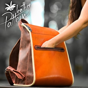Puede incluir: Una mochila de cuero marrón y naranja con un bolsillo con cremallera en la parte delantera. La mochila tiene un ribete blanco alrededor de los bordes.