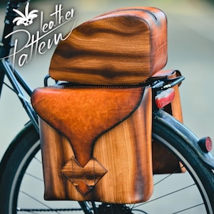 May include: A pair of brown leather bike panniers with wood accents attached to a black bicycle. The panniers have a flap closure and a decorative design on the front.