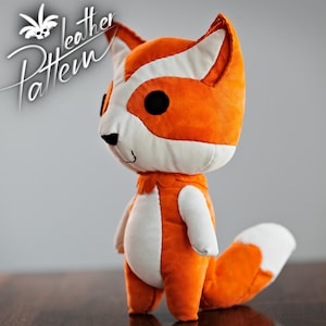 Könnte beinhalten: Ein Plüschtier in Form eines orangefarbenen und weißen Fuchses mit schwarzen Augen. Das Spielzeug steht auf einer Holzoberfläche.