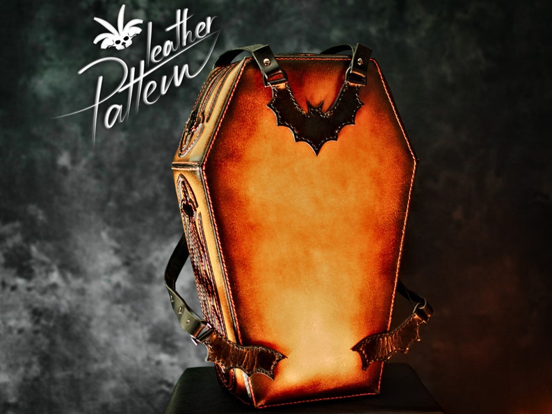 May include: A brown leather coffin-shaped backpack with a bat design on the front. The backpack has adjustable straps and a zip closure.