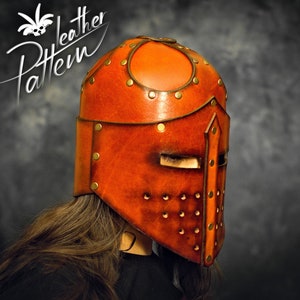 May include: A tan leather helmet featuring a central vertical ridge, a horizontal eye slit, and a series of small circular ventilation holes. The helmet is constructed with multiple panels joined by brass-colored metal rivets. Text reads Pattern Leather.