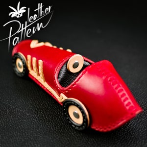 K&ouml;nnte beinhalten: Ein handgefertigtes rotes Leder-Rennauto mit beigen und schwarzen Akzenten. Das Auto hat ein detailliertes Design, einschlie&szlig;lich R&auml;dern und Cockpit. Das Bild enth&auml;lt auch den Text "leather Pattern".