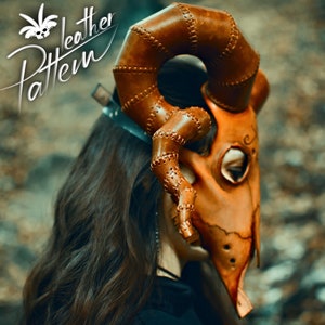May include: A brown leather mask with horns, stitched details, and a decorative design. The mask is worn by a person with long brown hair.