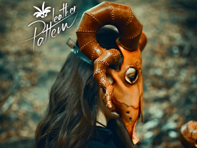 May include: A brown leather mask with horns, stitched details, and a decorative design. The mask is worn by a person with long brown hair.