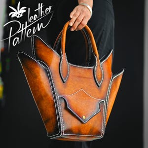 May include: A structured brown leather handbag with a gradient finish, featuring prominent pointed side panels, white contrast stitching, two top handles, and a central front pocket with a single brass-coloured stud. The text Leather Pattern is visible.