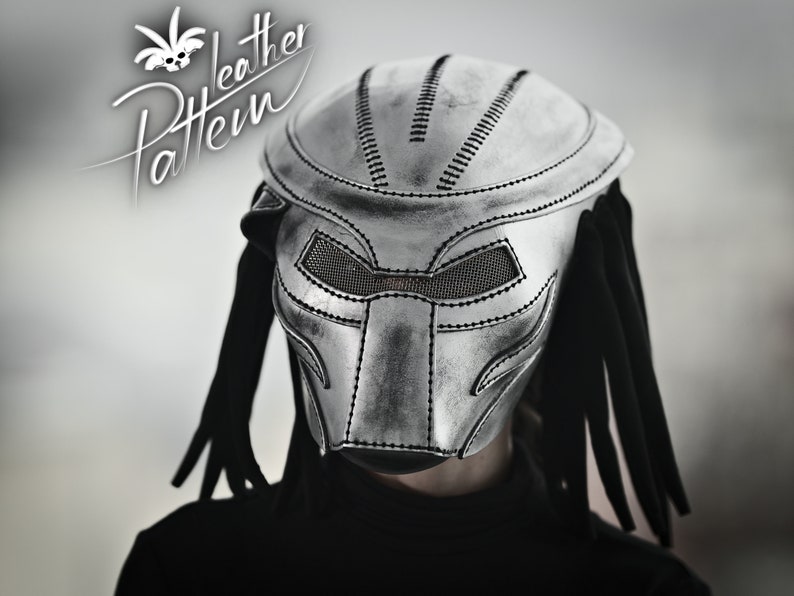 K&ouml;nnte beinhalten: Eine silberne Predator-Maske aus Leder mit schwarzen Dreadlocks. Die Maske hat ein detailliertes Design mit einem Netz, das die Augen bedeckt.