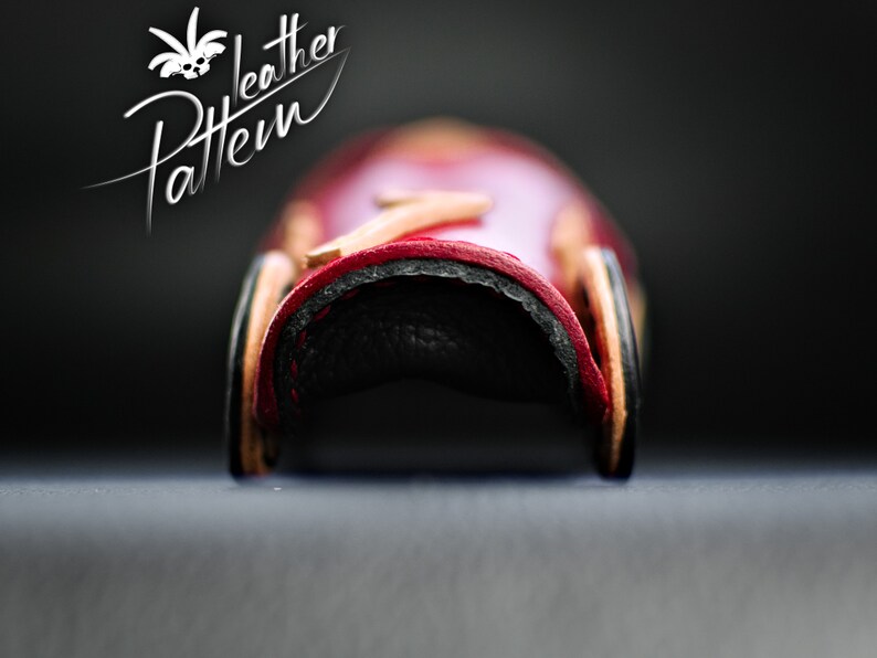 K&ouml;nnte beinhalten: Nahaufnahme eines Lederprodukts mit gebogener Form, in den Farben Rot, Schwarz und Hellbraun. Der Text "Leather Pattern" ist in wei&szlig;er Schrift zu sehen. Das Produkt scheint ein kleiner, handgefertigter Artikel zu sein.
