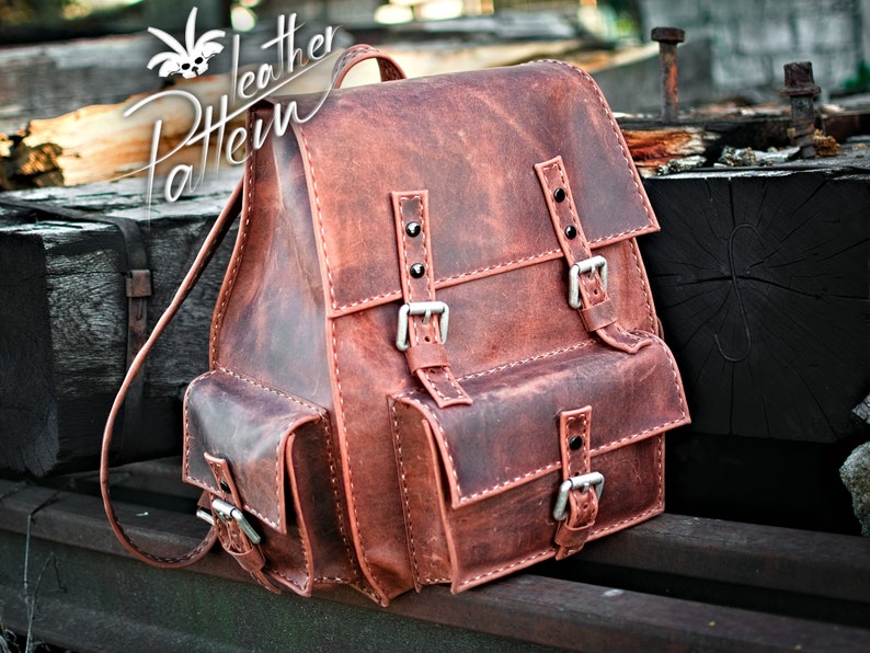 May include: A brown leather backpack with two large front pockets and two adjustable buckles. The backpack has a distressed look and is made of high-quality leather.