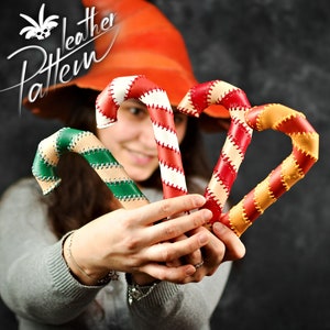 May include: Three handmade leather candy cane ornaments in red and white, green and white, and orange and white. The candy canes are held by a person wearing a grey sweater.