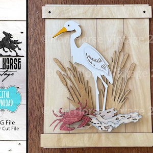 May include: A white egret bird standing in a bed of brown reeds with a red crab on a piece of driftwood at the bottom of the image. The image is a laser cut file for a wooden craft project.