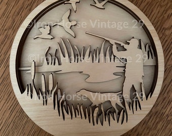 May include: A wooden wall art piece depicting a hunter with a shotgun aiming at ducks flying over a pond. The scene is set in a grassy marsh with cattails and a dog running in the background.